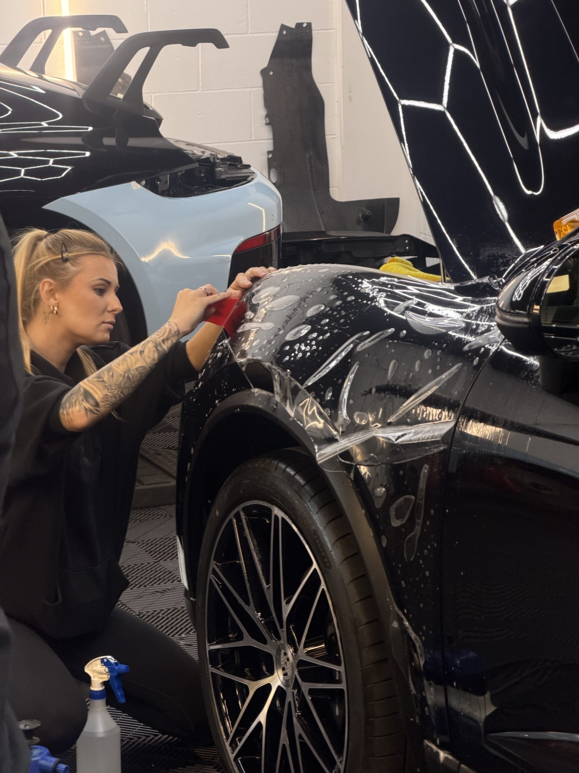 Fitter applying protective film to a black car's front wing