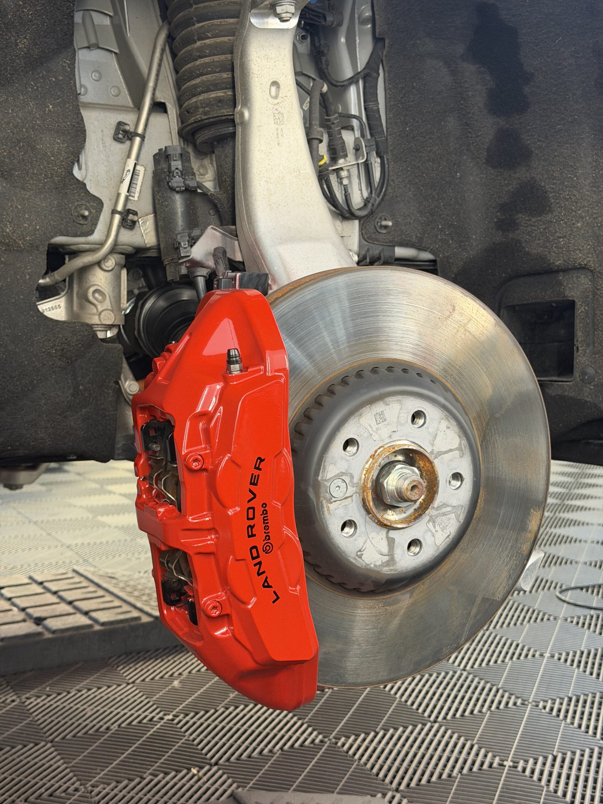 Red painted brake caliper on a car with the wheel removed
