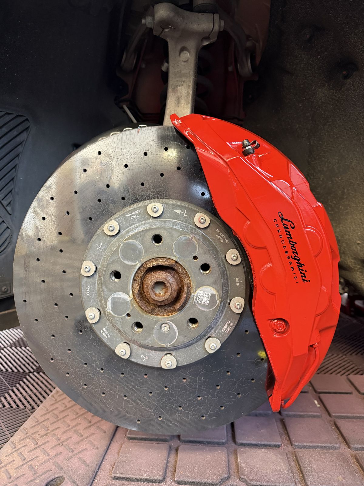Close-up of a Lamborghini Urus brake caliper painted red, with drilled carbon-ceramic disc