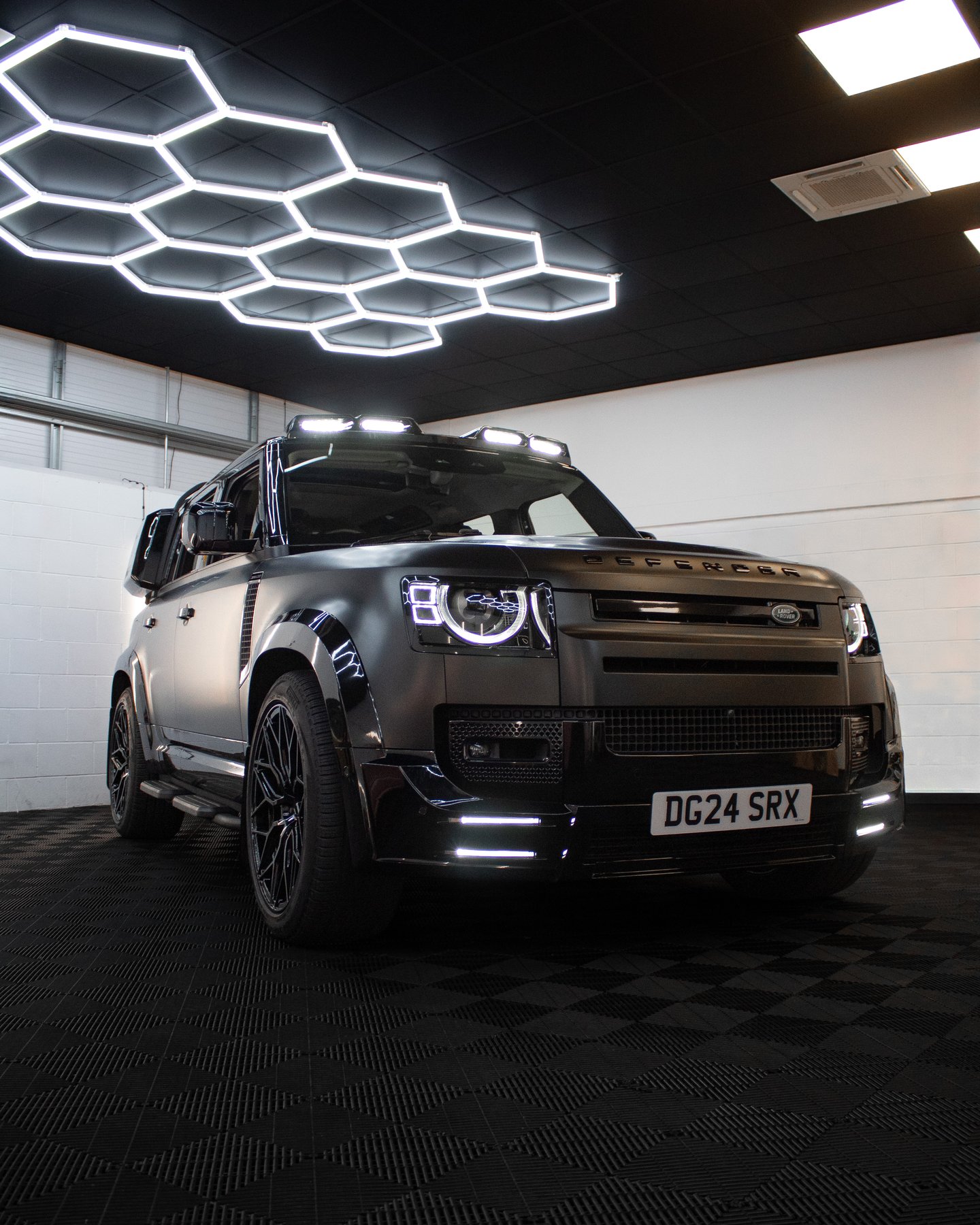 Satin black Land Rover Defender 110 under the hexagon ceiling lights in the Wrapd Studios workshop in Knaresborough